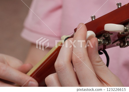 Extreme close-up of female fingers tuning acoustic guitar, tightening and loosening strings 123226615