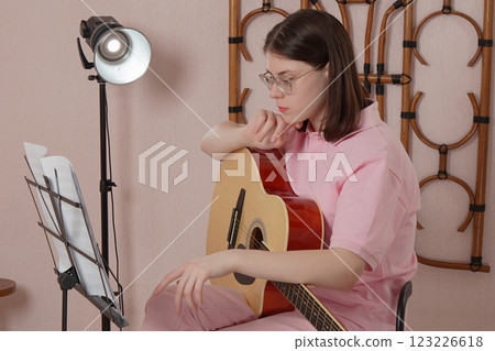 Woman with guitar sets up sheet music on music stand before playing acoustic guitar in home studio 123226618