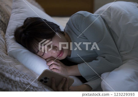 A woman watching a smartphone in bed A woman watching a smartphone in bed 123229393