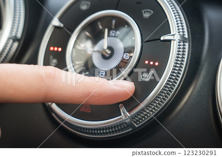 Turning on the three-level seat heating in the car, the finger presses the button. A closeup image featuring a finger skillfully adjusting the temperature controls on a modern cars sleek dashboard. 123230291