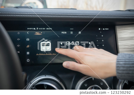 A detailed closeup view of a cars touchscreen dashboard displaying radio tuning and an engaging user interaction. Setting up the radio and media system on the touchpad with your hand and finger on the 123230292
