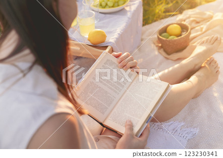 A woman is peacefully reading a book at an outdoor picnic with food on a sunny day 123230341