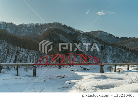 A train crossing a red iron bridge in a snowy valley 123230403