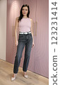 Pretty brunette 51 years old in pink high-heeled shoes in a pink fashionable T-shirt and grey jeans posing near a pink wardrobe 123231414