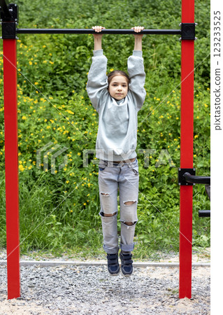 Young girl training on a pull-up bar in a park surrounded by greenery 123233525