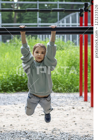 Young girl practicing on horizontal bars outdoors in recreational park area Young girl practicing on horizontal bars outdoors in recreational park area 123233526