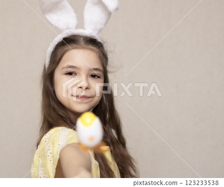 Smiling girl wearing bunny ears holding Easter egg in bright yellow setting 123233538