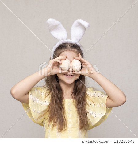Smiling girl wearing bunny ears holding eggs in a playful pose for Easter Smiling girl wearing bunny ears holding eggs in a playful pose for Easter 123233543