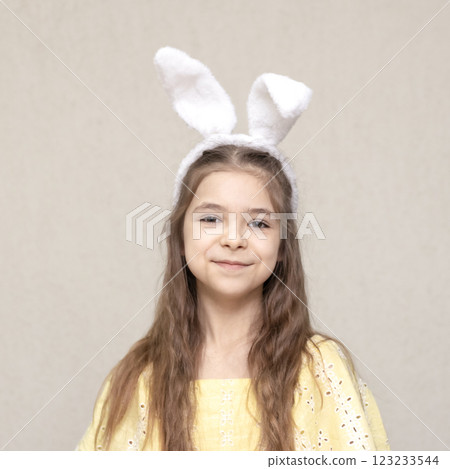 Young girl wearing bunny ear headband smiling and posing against a light background 123233544