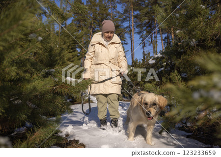 Elderly woman walking a Golden Retriever in a snowy forest on a sunny winter day, enjoying nature and fresh air. Elderly woman walking a Golden Retriever in a snowy forest on a sunny winter day, enjoying nature and fresh air. 123233659