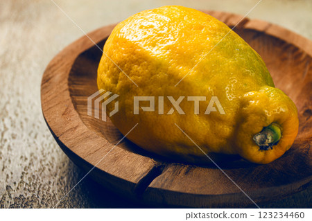 Bright yellow lemon resting on a wooden dish illuminated by soft light in a cozy kitchen setting 123234460