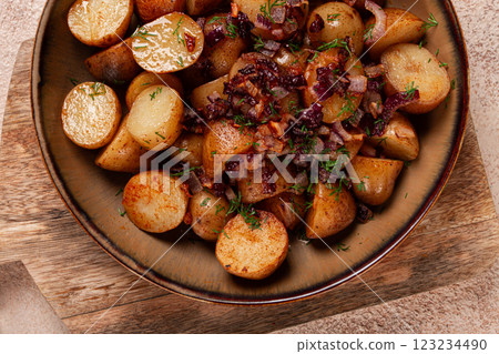 Delicious roasted potatoes garnished with caramelized onions and fresh herbs served in a rustic bowl 123234490