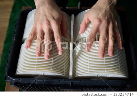Hands are carefully handling industrial filters while inside a well-organized storage box 123234714