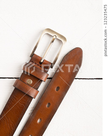 Brown genuine leather belt on a white wooden background. 123235475