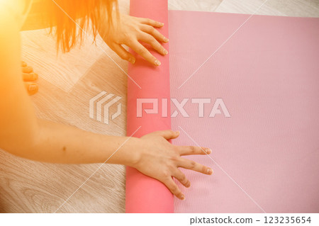 A young woman rolls a pink fitness or yoga mat before or after exercising, exercising at home in the living room or in a yoga studio. Healthy habits, keep fit, weight loss concept. Closeup photo 123235654