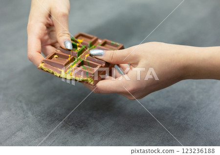Female hands breaking off piece of Dubai chocolate on gray background. Green kadayif and pistachio spread with pistachio in trend dessert. Close-up, selective focus. High quality photo Female hands breaking off piece of Dubai chocolate on gray background. Green kadayif and pistachio spread with pistachio in trend dessert. Close-up, selective focus. High quality photo 123236188