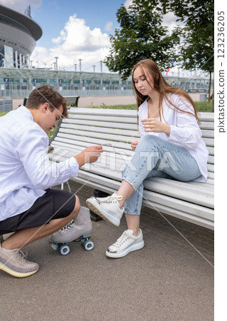 Man helps to tie laces on quad rollers. Young couple rollerblading in park. Vertical photo. High quality photo Man helps to tie laces on quad rollers. Young couple rollerblading in park. Vertical photo. High quality photo 123236205