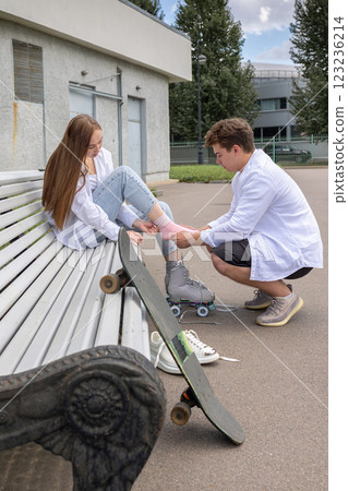 Man helps to tie laces on quad rollers. Young couple rollerblading in park. Vertical photo. High quality photo Man helps to tie laces on quad rollers. Young couple rollerblading in park. Vertical photo. High quality photo 123236214
