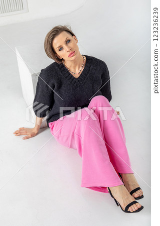 Portrait beautiful woman of model appearance. Girl in black jumper and pink trousers on grey background. Pretty female with trendy makeup posing in studio. Vertical photo.  Portrait beautiful woman of model appearance. Girl in black jumper and pink trousers on grey background. Pretty female with trendy makeup posing in studio. Vertical photo.  123236239