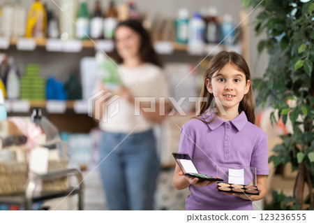 Little girl longingly looks at eye shadow pallet in shop and dreams of makeup like adult lady Little girl longingly looks at eye shadow pallet in shop and dreams of makeup like adult lady 123236555