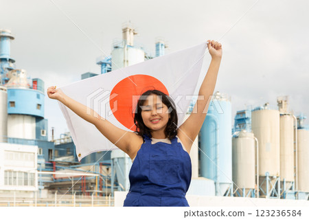 Happy young woman with flag of Japan against background of factory Happy young woman with flag of Japan against background of factory 123236584