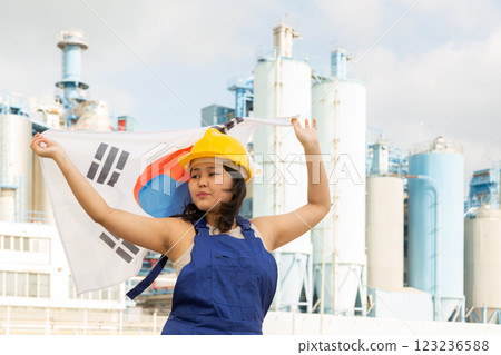 Happy asian girl in work clothes and hardhat with flag of south korea standing in front of industrial scenery Happy asian girl in work clothes and hardhat with flag of south korea standing in front of industrial scenery 123236588
