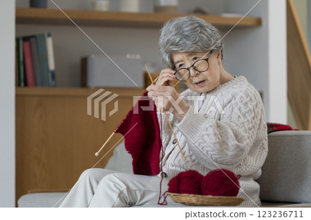Senior woman pushes her glasses aside to look at her knitting stitches 123236711