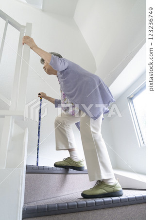 A senior woman walking up the stairs with a cane and holding onto the handrail 123236749