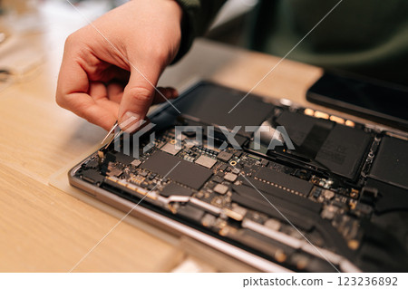 Close-up of skilled technician using tweezers assembling component on laptop motherboard, performing maintenance and troubleshooting in repair workshop. Concept of process electronic device repair. 123236892