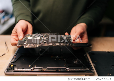 Electronic technician carefully handling delicate computer motherboard during precision laptop repair at professional workbench. Concept of computer hardware, repairing, upgrade and technology. 123236893