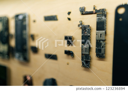 Disassembled smartphones displayed on wooden wall, exposing complex internal electronics and circuitry during professional technical diagnostic procedure in modern repair workshop, close-up 123236894