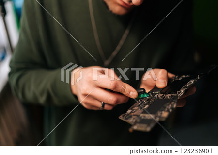 Cropped shot of unrecognizable technician male carefully cleaning laptop motherboard with a small brush. Concept delicate process of hardware maintenance in workshop environment. 123236901