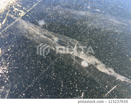A close-up view of a frozen surface with visible cracks and bubbles, capturing the intricate details and natural patterns of the ice. 123237630