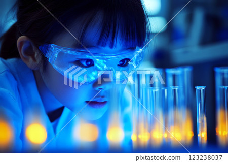 A child wearing goggles closely examines glowing test tubes, highlighted by a blue light. 123238037