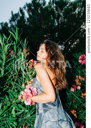 Young caucasian female relaxing in garden with pink flowers and greenery Young caucasian female relaxing in garden with pink flowers and greenery 123238683