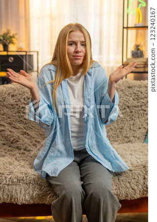 Young woman clueless shrug at home, arms spread, doubt, uncertain look, confused mood, no answer 123240167