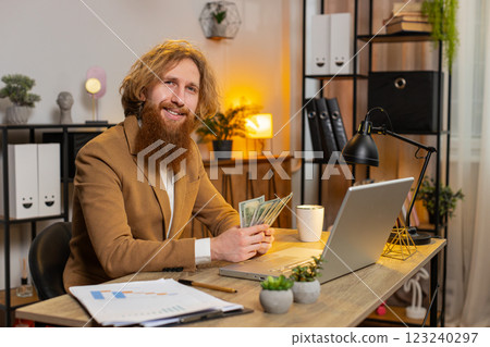Successful rich businessman counting money cash calculates dividends and using laptop in home office 123240297