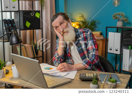 Tired exhausted senior man freelancer analyzing paperwork graphs accounting payments bank bills 123240311
