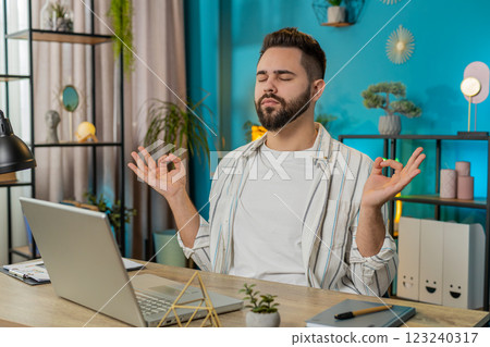 Peaceful relaxed businessman sitting at workplace with folded in mudra gesture hands meditating Peaceful relaxed businessman sitting at workplace with folded in mudra gesture hands meditating 123240317