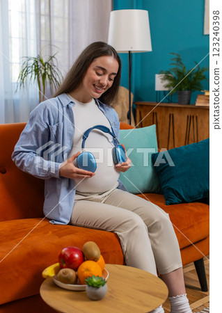 Pregnant woman sitting on home sofa listening music putting headphones on her tummy with child baby Pregnant woman sitting on home sofa listening music putting headphones on her tummy with child baby 123240398
