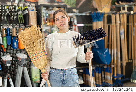 Girl in hardware store examines broom and besom. Girl in hardware store examines broom and besom. 123241241