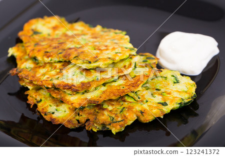 Zucchini pancakes with sour cream on black plate Zucchini pancakes with sour cream on black plate 123241372