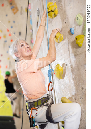 positive muscular retired woman in gym climbing up artificial rock climbing wall positive muscular retired woman in gym climbing up artificial rock climbing wall 123241672