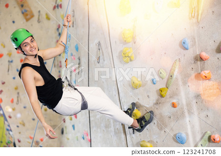 Determined young man in safety helmet doing his best at climbing artificial wall Determined young man in safety helmet doing his best at climbing artificial wall 123241708