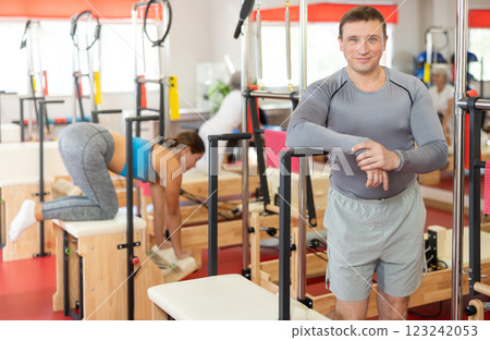Positive man coach stands in large gym against background of Pilates simulators 123242053