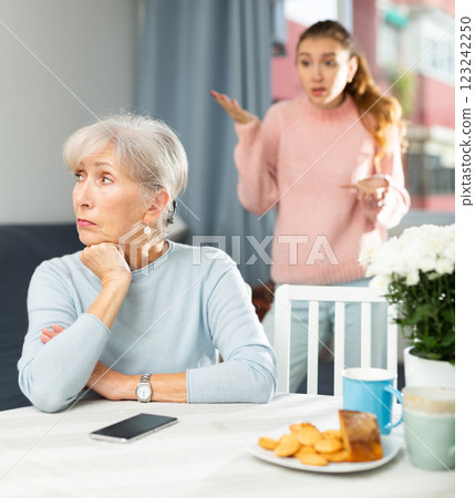 Worried adult daughter scolding upset elderly woman at table Worried adult daughter scolding upset elderly woman at table 123242250
