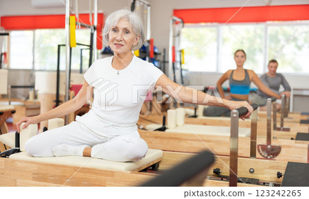 Senior woman performs exercise on reformer to improve coordination, balance, and posture Senior woman performs exercise on reformer to improve coordination, balance, and posture 123242265