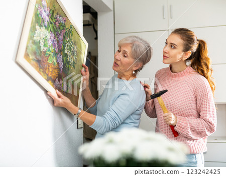 Senior woman and granddaughter trying to put picture on wall 123242425