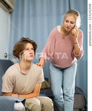 Teenager suffering from stomach pain while mother speaking on phone Teenager suffering from stomach pain while mother speaking on phone 123242446