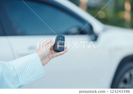 Hand holding car remote control, smart key to lock or unlock doors of white car. Safety, travel and transportation concept Hand holding car remote control, smart key to lock or unlock doors of white car. Safety, travel and transportation concept 123243396